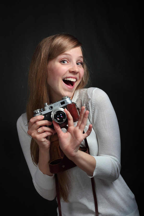 She does like cameras | camera, black background, smile, white shirt