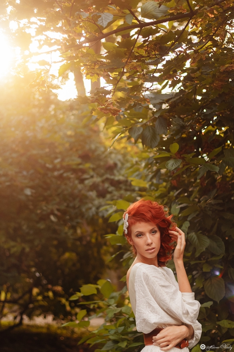 Environmental portrait of a red-haired woman | portrait, model, woman, red-haired, white dress, hair-do, natural make-up, trees, green, sunshine