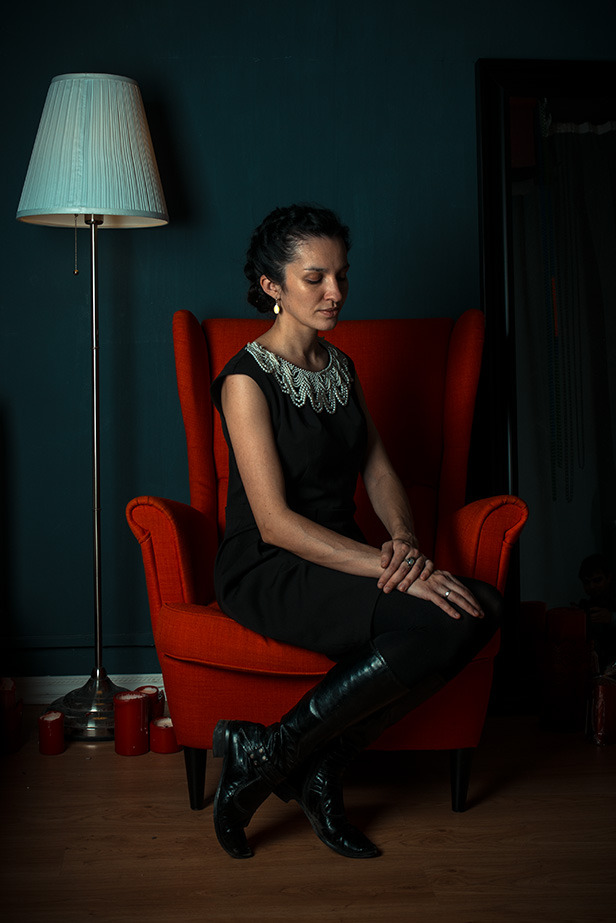 Sad woman in a red armchair | portrait, model, woman, brunette, room, red armchair, floor lamp, black dress, candles, sad